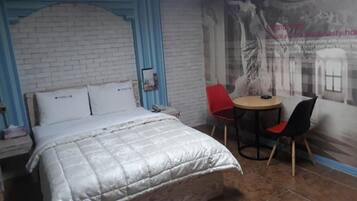 Un dormitorio con una cama, una mesita pequeña con dos sillas y un mural en la pared.