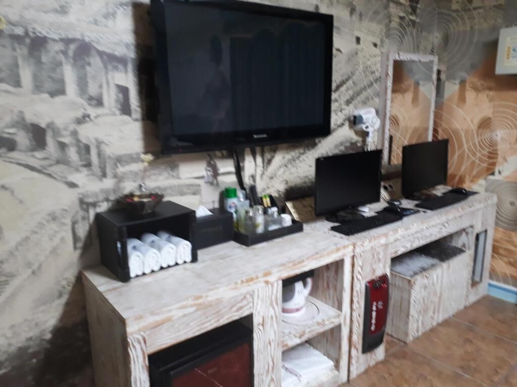 A room with a television mounted on a textured wall, a wooden cabinet with various items, and a speaker on the right.