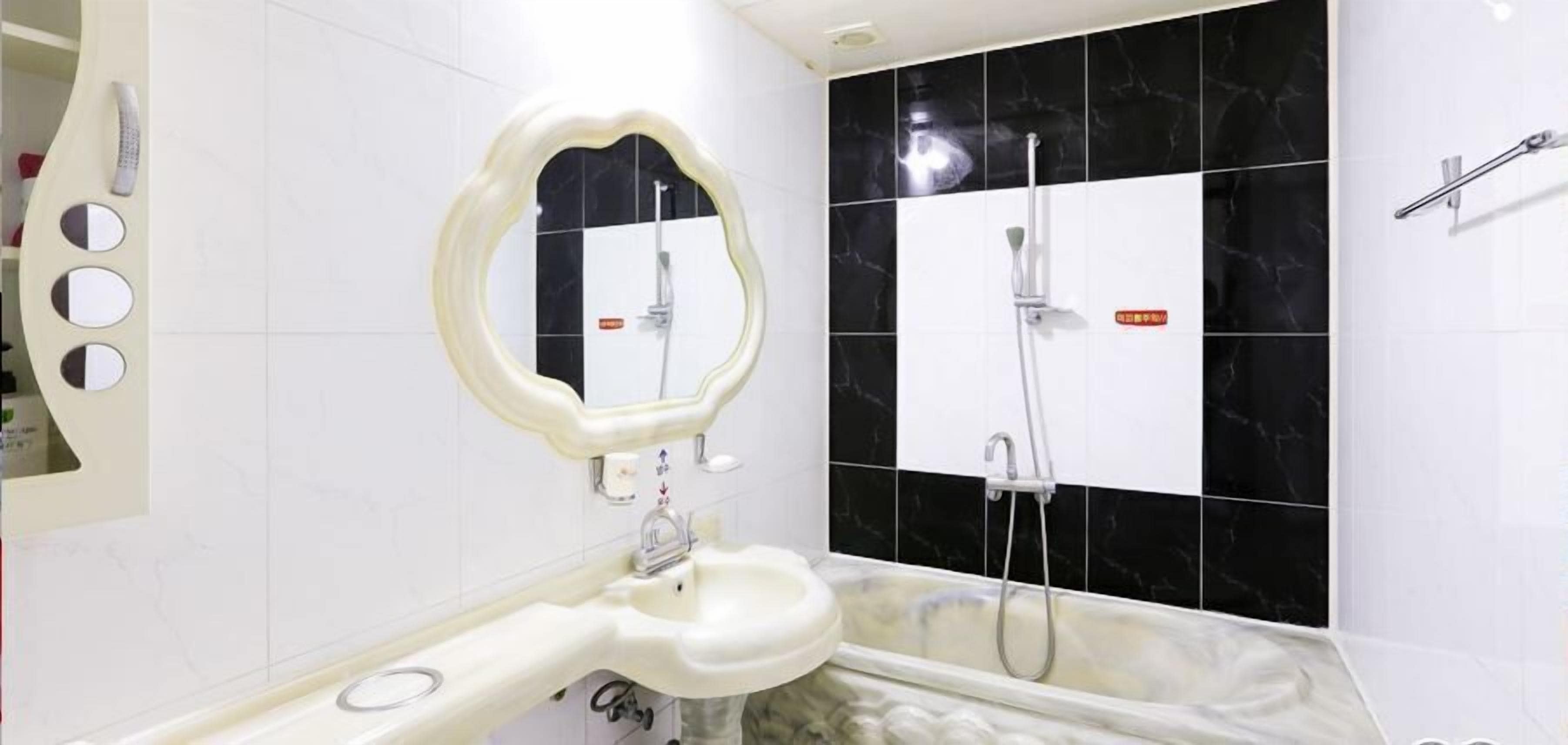 Un bany amb un lavabo blanc, un mirall, una dutxa i parets revestides de rajoles negres i blanques.