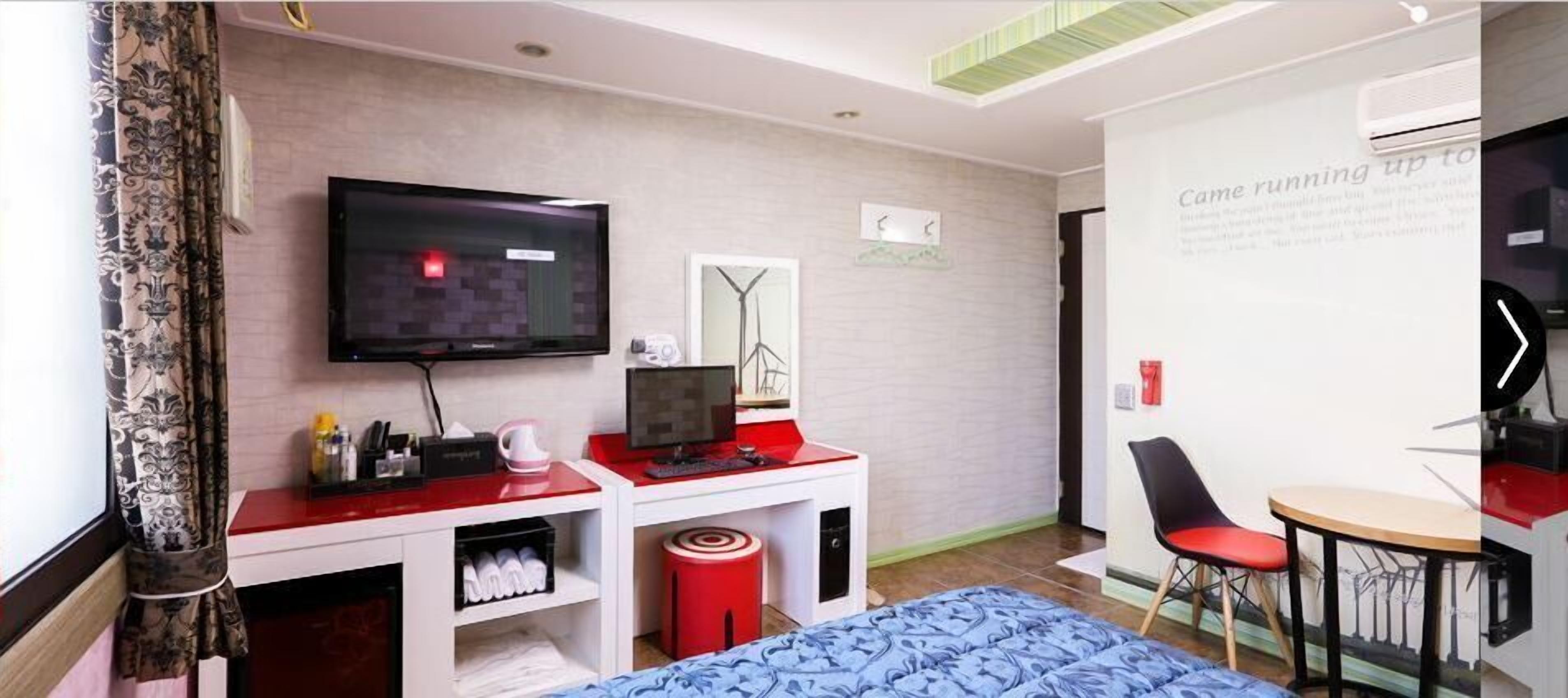 Een hotelkamer met een bed, een bureau met een computer, een televisie, een stoel en een klein tafeltje.