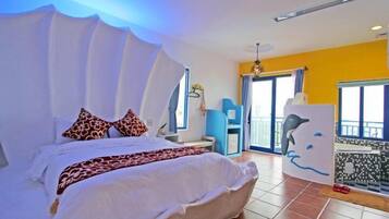 Un dormitorio con cama, almohadas, una mesita de noche, una ventana y un balcón con un mural de delfines.