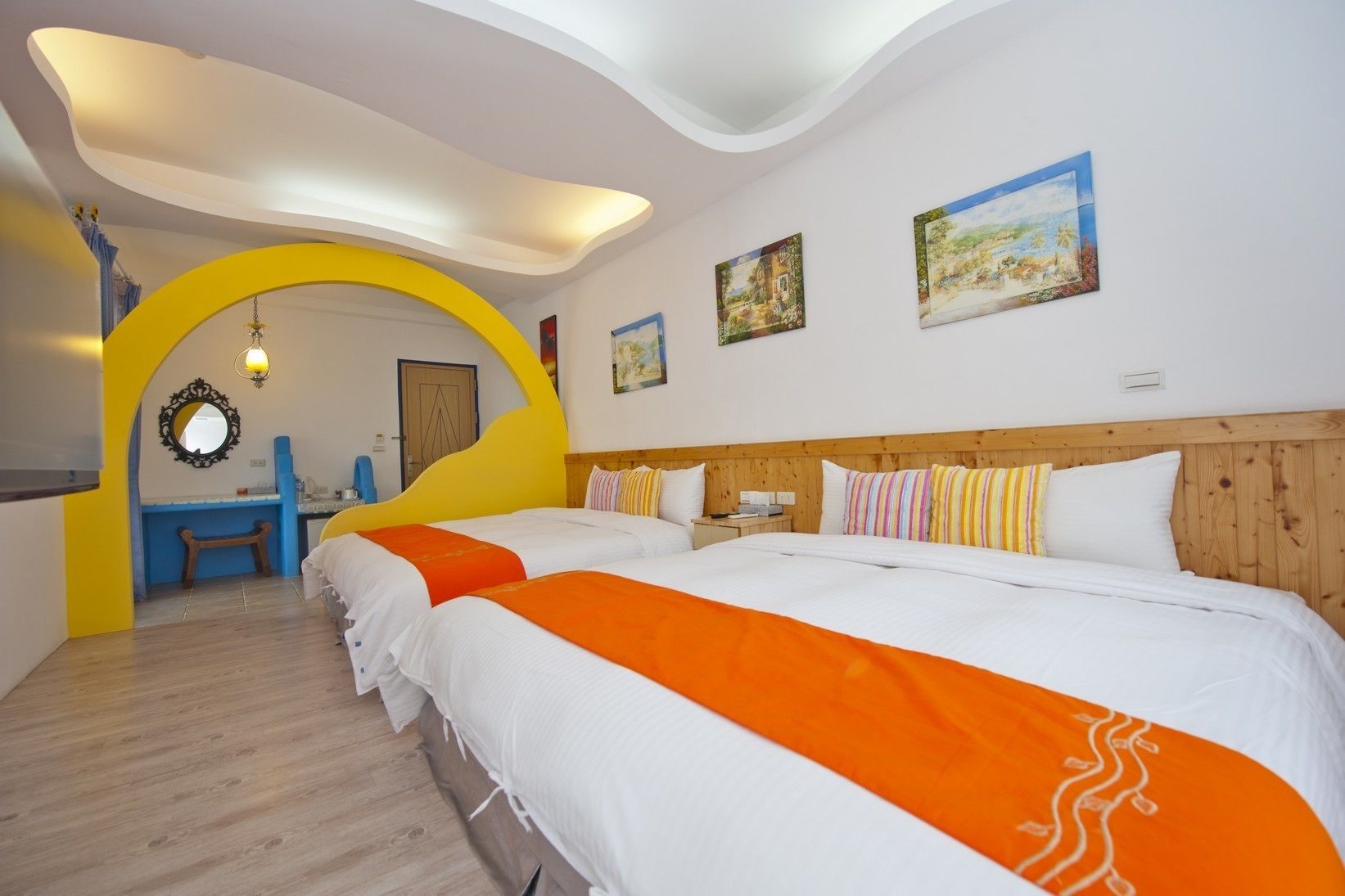 A hotel room with two beds, a wooden headboard, a yellow archway, and a painting on the wall.