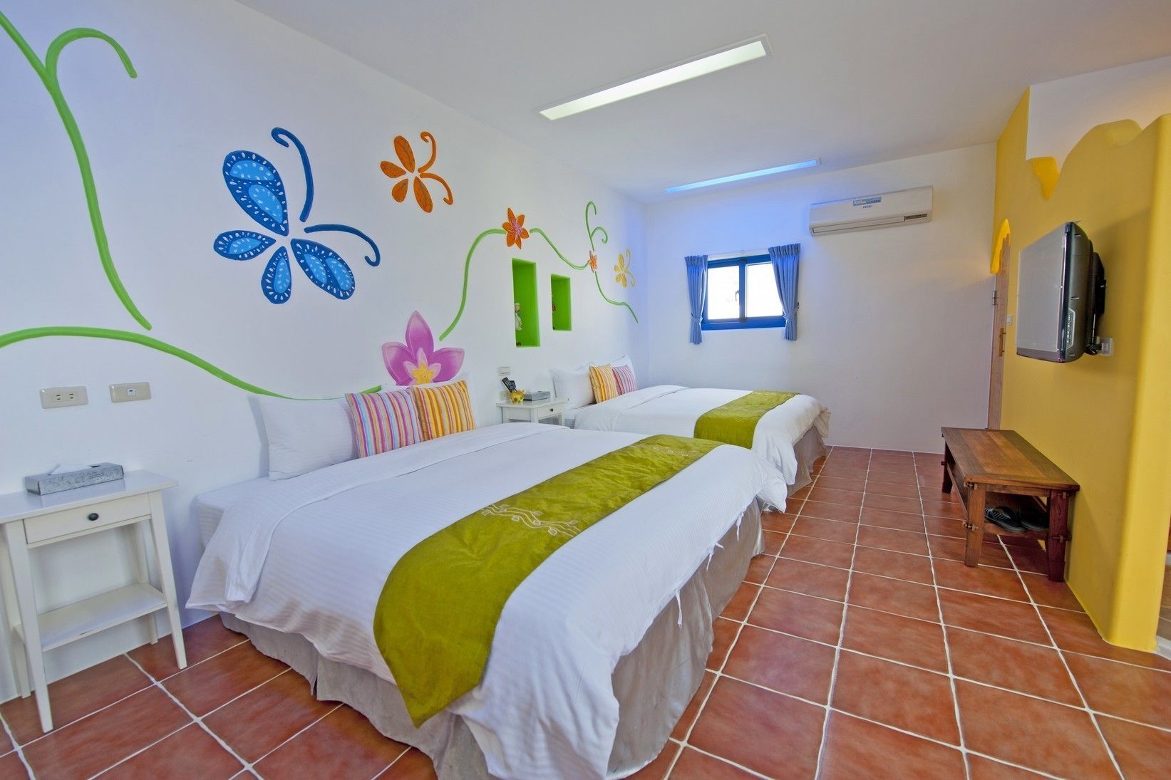 Una habitación de hotel con dos camas, una mesita, un televisor y una ventana con cortinas.