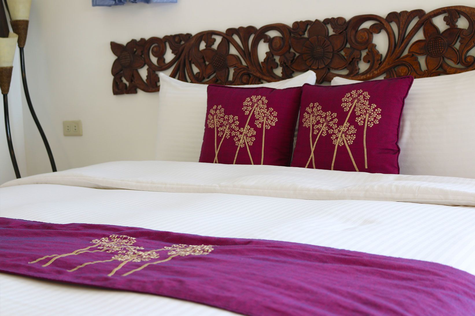 Una cama bien hecha con sábanas blancas y dos almohadones decorativos con motivos florales.