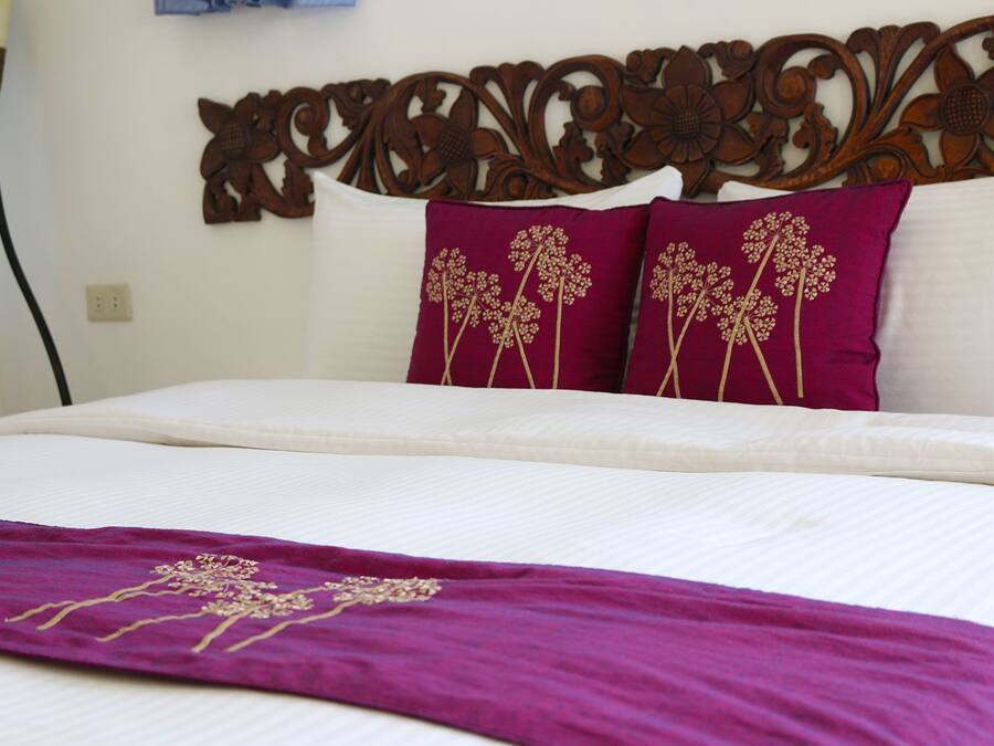 Una cama bien hecha con sábanas blancas y dos almohadones decorativos con motivos florales.