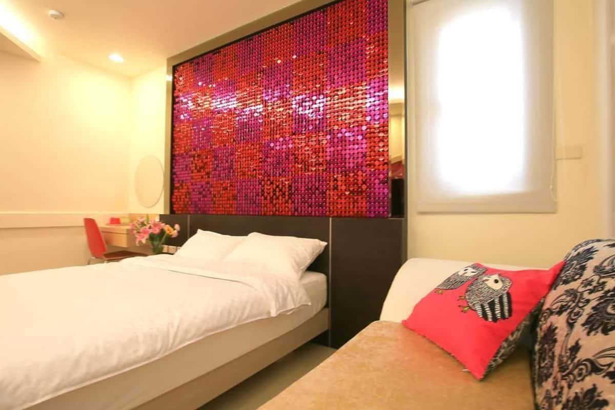 A hotel room with a bed, a bedside table, a red decorative panel, and a window.