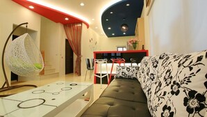 A modern living room with a sofa, a hanging chair, a dining area with a red table, and a staircase. - Amethyst Bay (Magong)