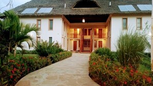 Une maison à deux étages, dotée d’un toit de chaume, de panneaux solaires et d’un chemin de pierre menant à l’entrée.