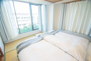 A hotel room with a bed, large windows, and a view of buildings outside.