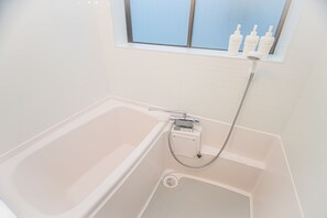 A modern bathroom with a bathtub, a handheld showerhead, and a window with bottles on the sill.
