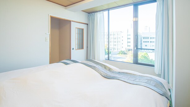 A hotel room with a large bed, a window with curtains, and a door. - AMP FLAT Nishijin5 (Fukuoka)