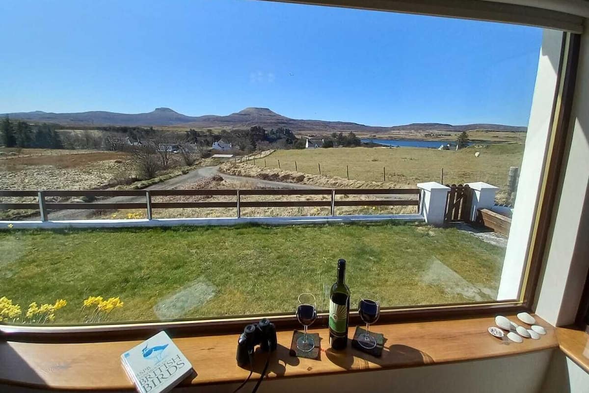 A view from inside a vehicle, looking out through a window at a rural landscape with fields, a fence, and a distant hill.