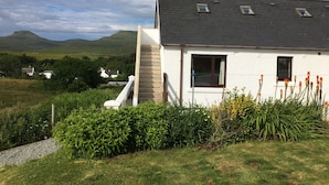 Une maison blanche avec un toit gris, une petite fenêtre et un escalier menant à l’entrée.