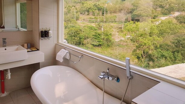 A bathroom with a bathtub, a sink, and a window offering a view of a green landscape. - Moonshine B&B (Touwu)