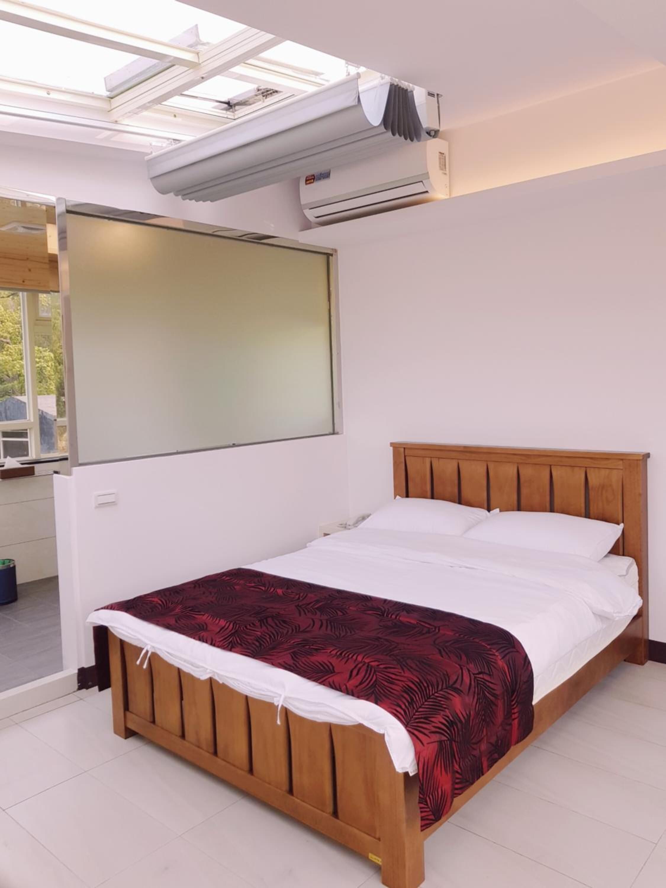 Un lit simple avec une tête de lit en bois, une couvre-lit rouge à motifs et un appareil de climatisation fixé au mur au-dessus.
