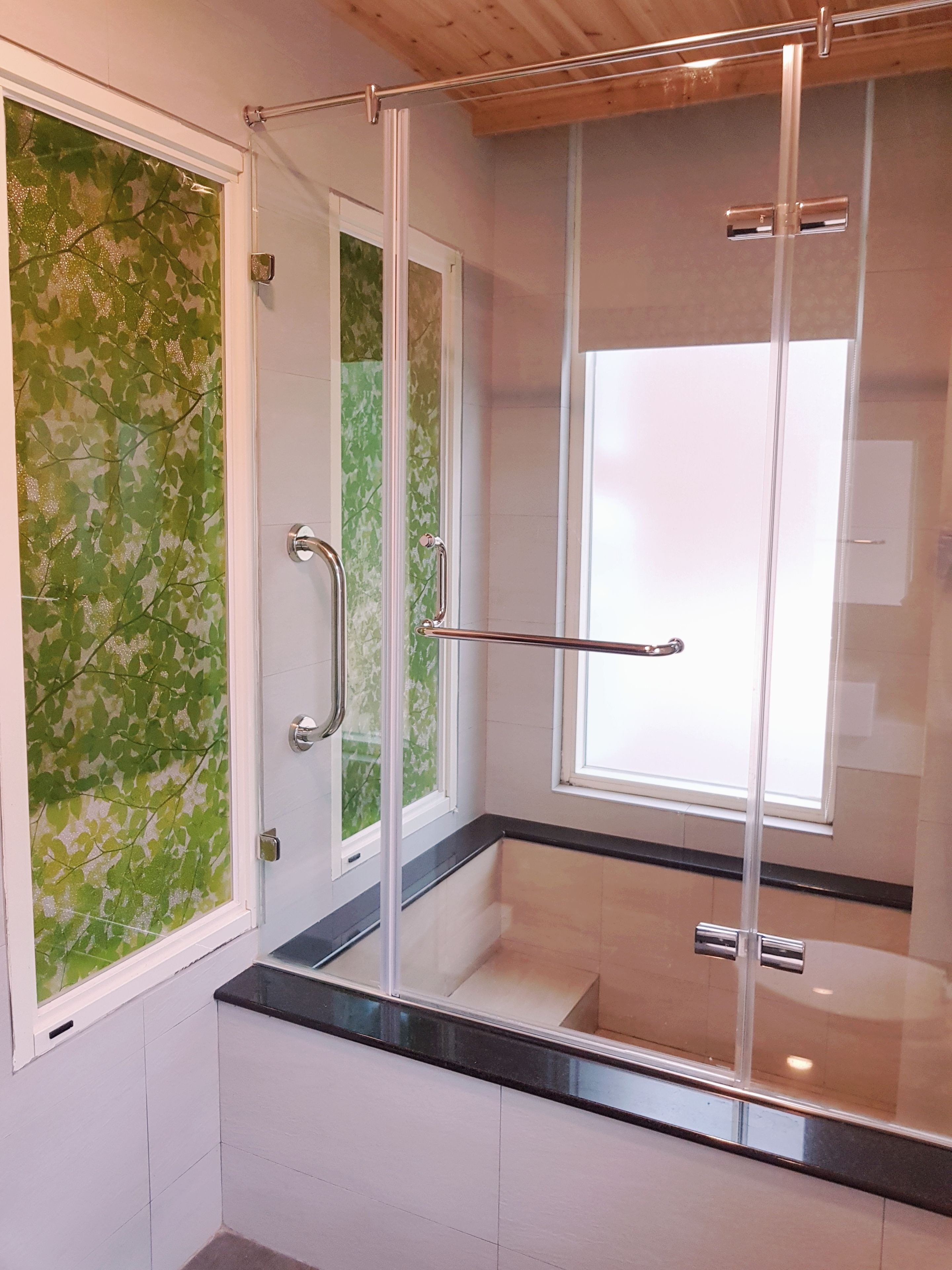 A modern shower enclosure with glass doors, a metal handle, and a window.