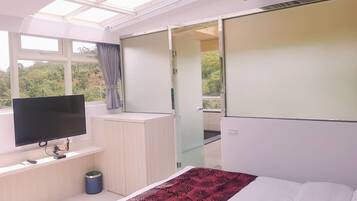 Un dormitorio moderno con una cama grande, un televisor en un mueble empotrado, una puerta corrediza que da a un balcón y un tragaluz arriba.