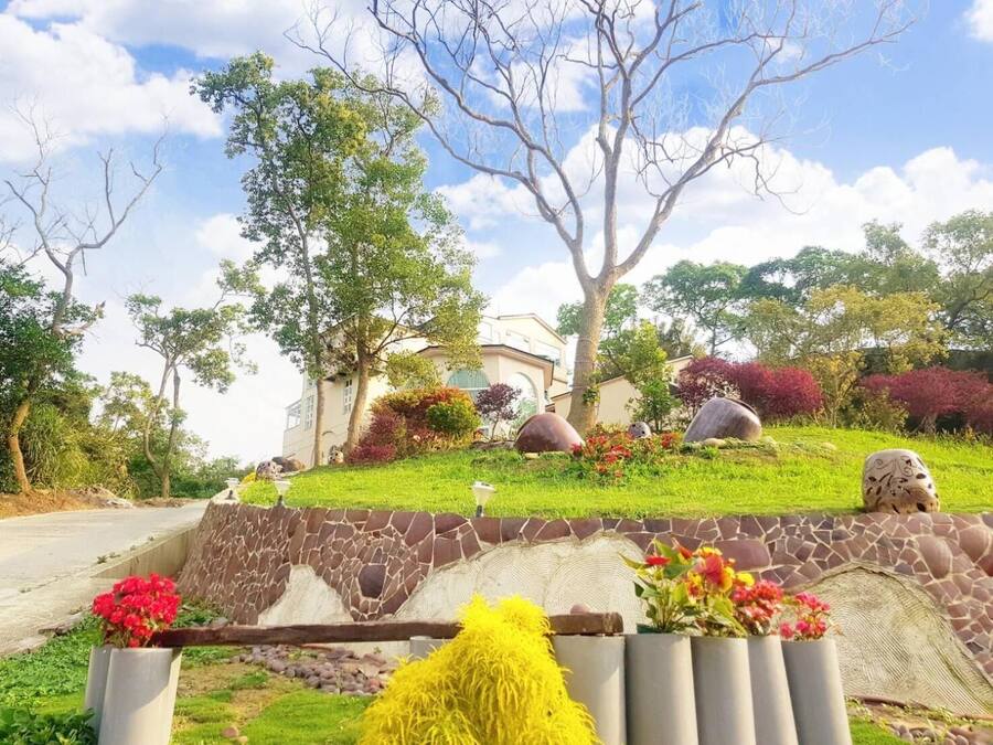 A landscaped garden with a stone wall, various plants, and a house in the background.