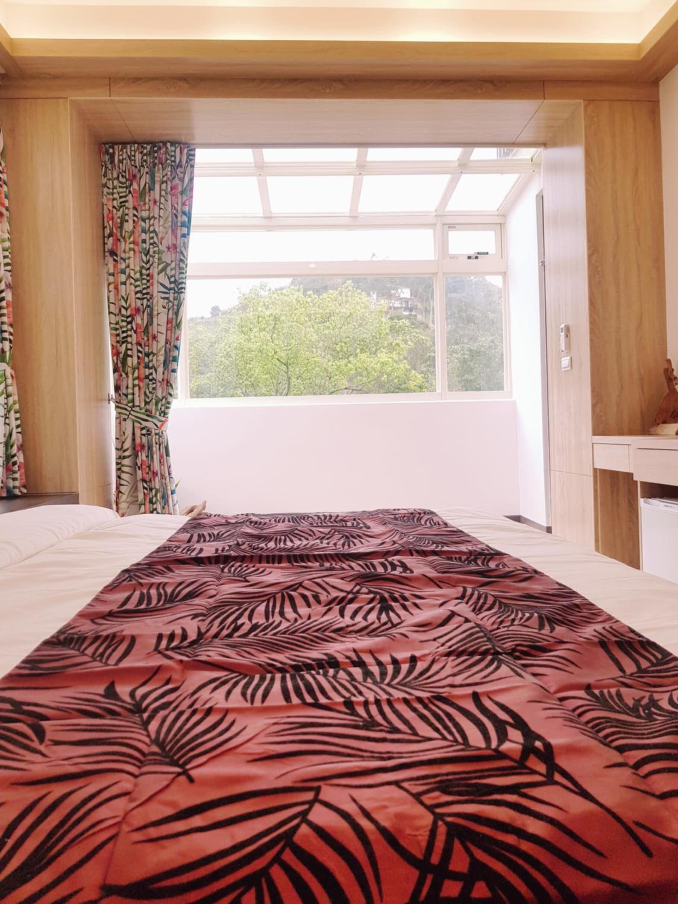 Un dormitorio con un ventanal grande, una cama con colcha de diseño rojo y negro, y vistas a árboles fuera.
