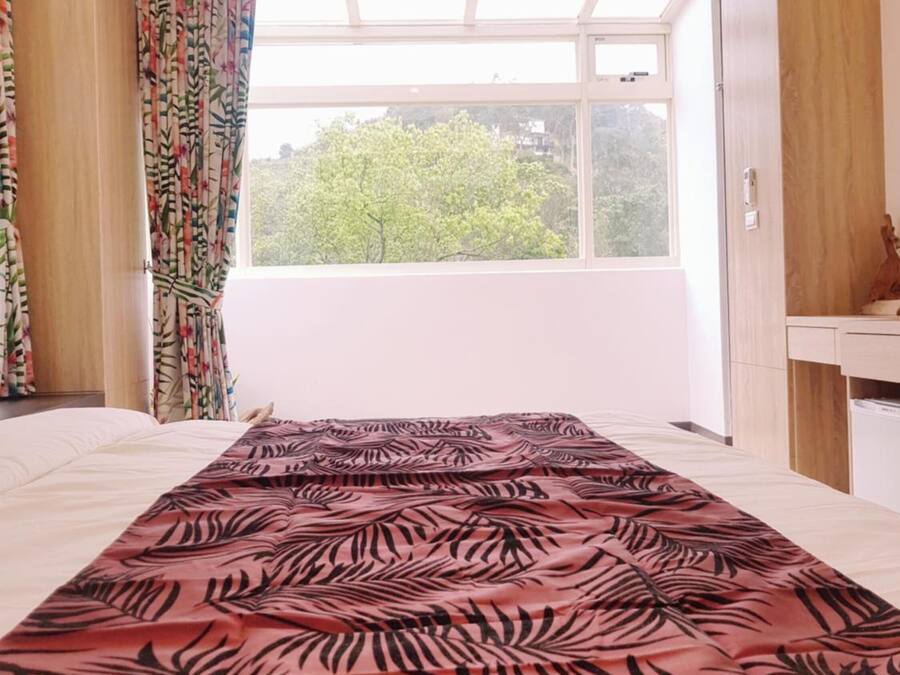Un dormitorio con un ventanal grande, una cama con colcha de diseño rojo y negro, y vistas a árboles fuera.