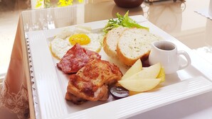 A breakfast tray with eggs, bacon, toast, and fruit on a table near a window with a view of buildings and a plant outside. - Moonshine B&B (Touwu)