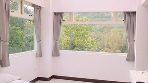 A bedroom with a large bed, two windows with curtains, a skylight, and a view of greenery outside. - Moonshine B&B (Touwu)
