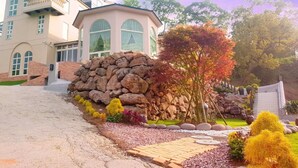 A large, two-story house with a stone wall and a garden with various plants and a paved walkway. - Moonshine B&B (Touwu)