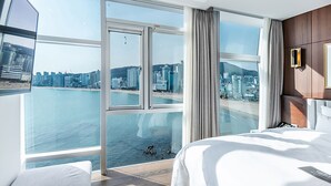 Camera d'albergo con un'ampia finestra vista sulla città, un letto e una zona salotto.