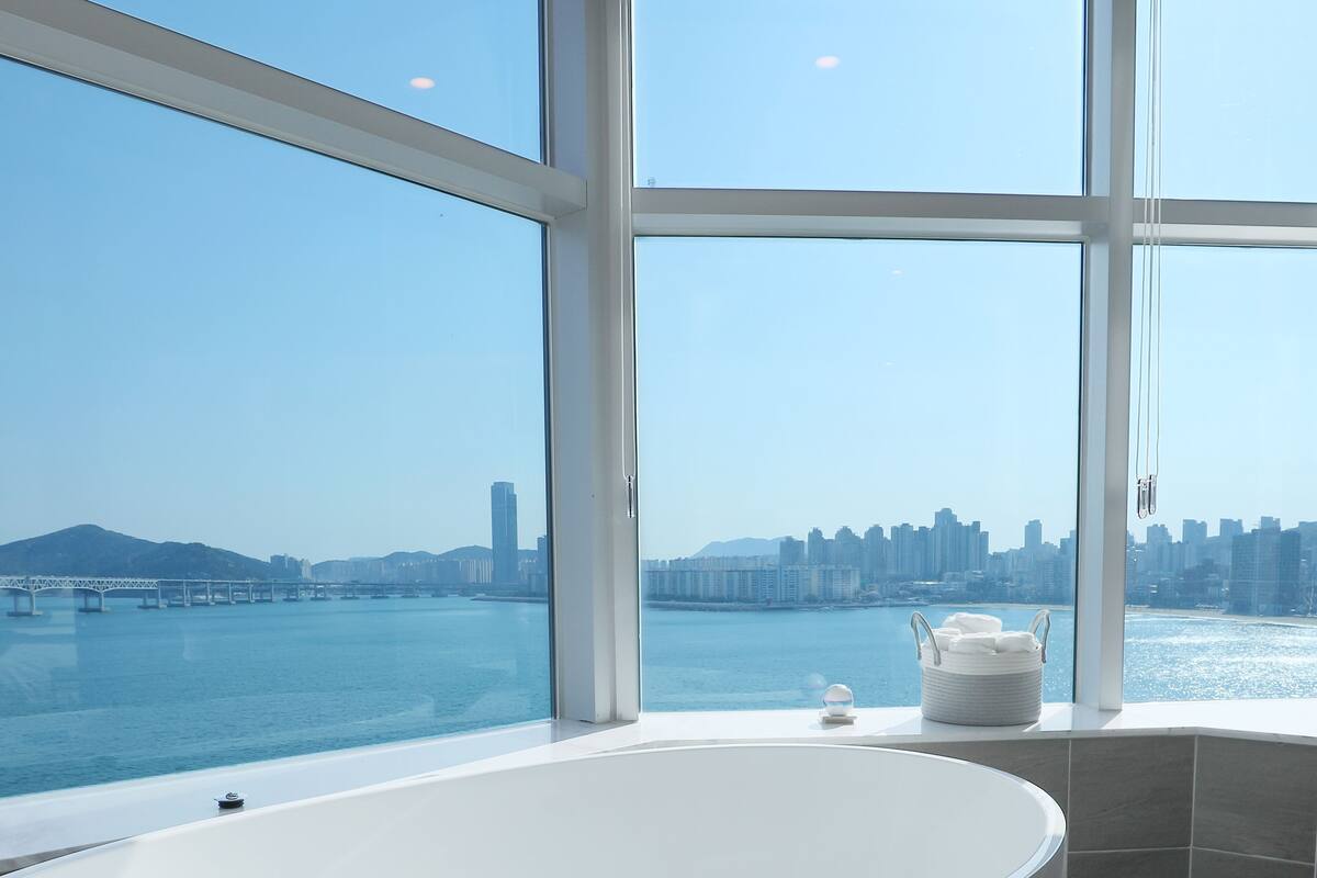 A modern bathroom with a large bathtub, a view of a city skyline, and a body of water.