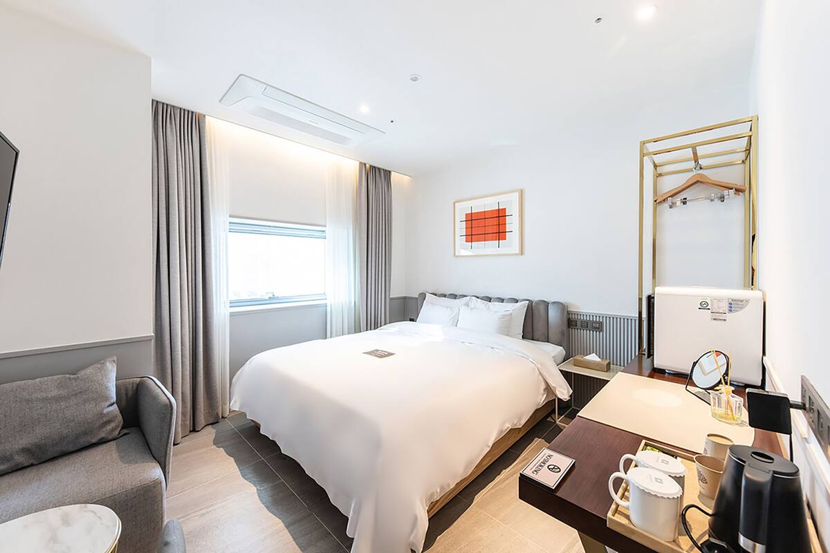 A hotel room with a bed, a desk with a coffee maker, a mirror, and a window with curtains.