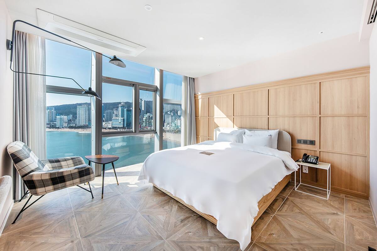 A modern hotel room with a large bed, a view of the city, and a balcony with a pool.