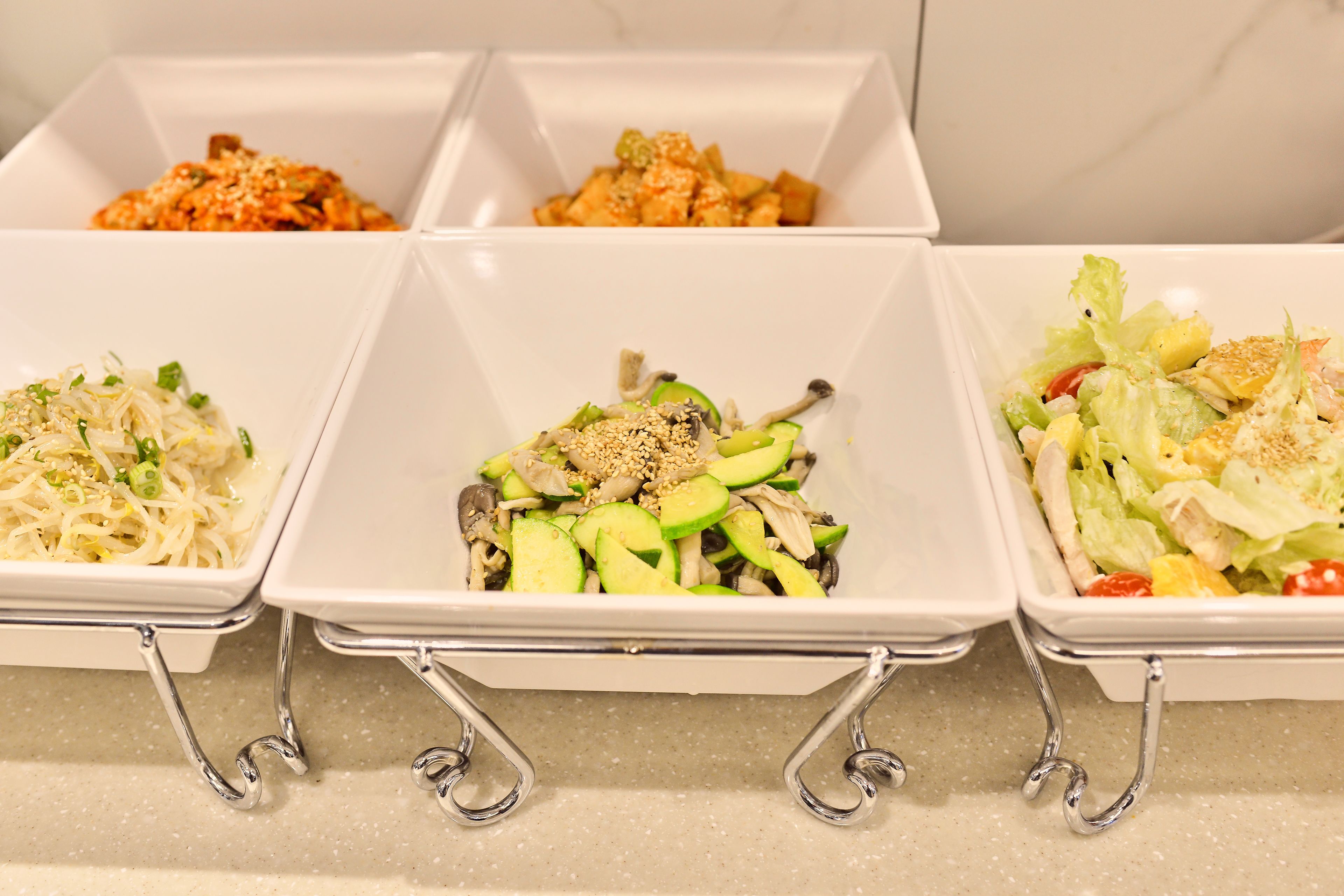 Three white square dishes with metal handles on a countertop.