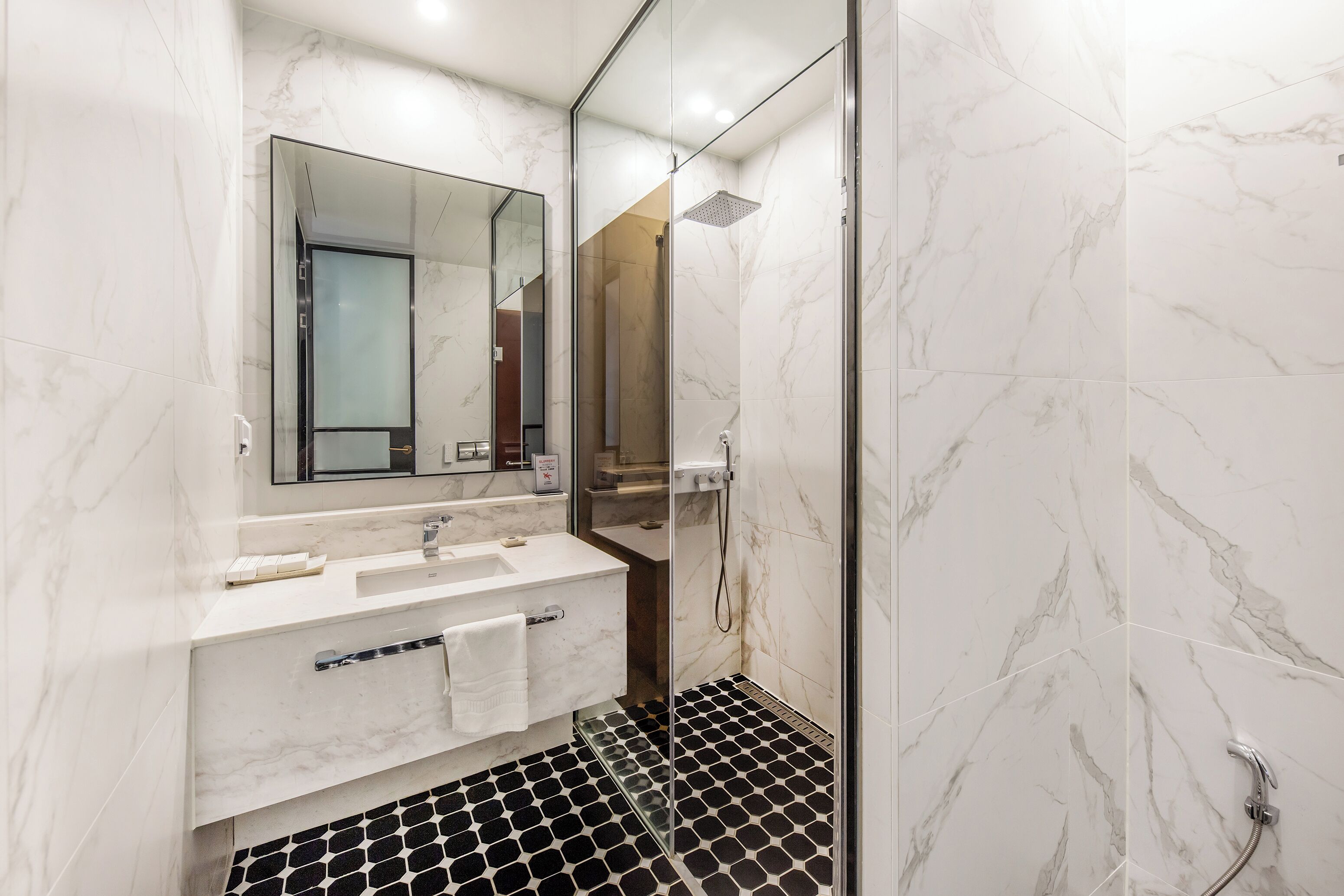 Een moderne badkamer met een douchecabine van glas, een grote spiegel en een zwart-wit betegelde vloer.