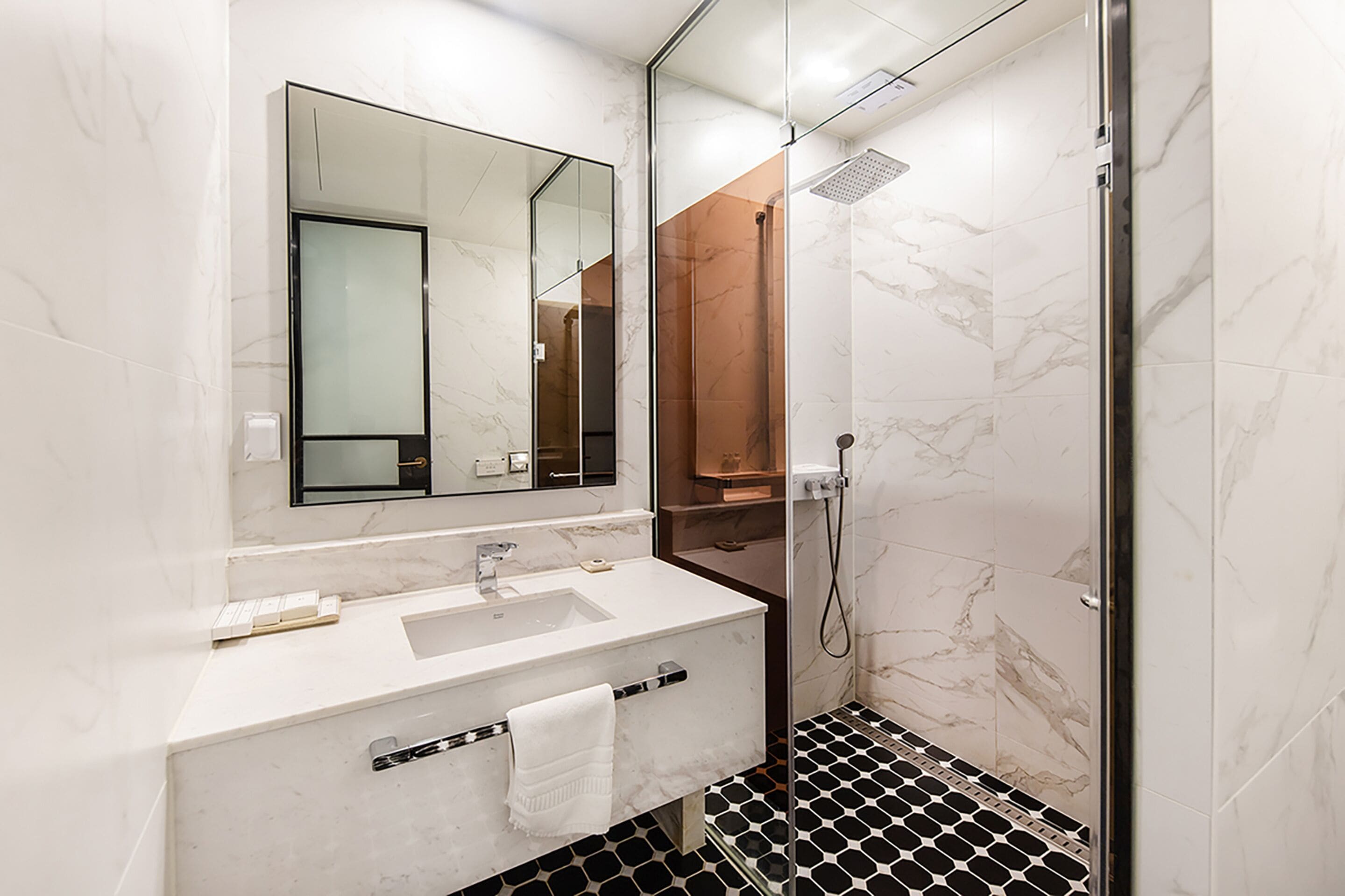 Un baño moderno con un lavamanos blanco, un espejo grande y una ducha con mampara de vidrio.