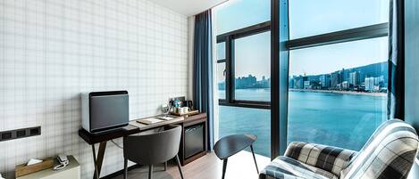 A modern hotel room with a city view, a desk with a computer, a chair, and a bed.