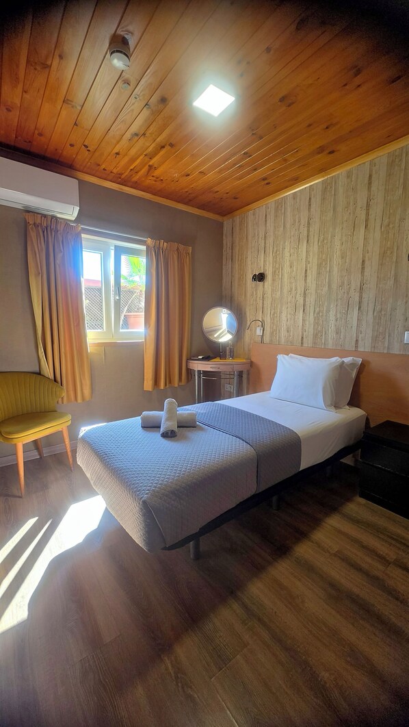 A room with a bed, a bedside table with a lamp, a chair, and a window with curtains.