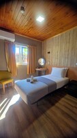 Una habitación con cama, mesita de noche con lámpara, una silla y una ventana con cortinas.