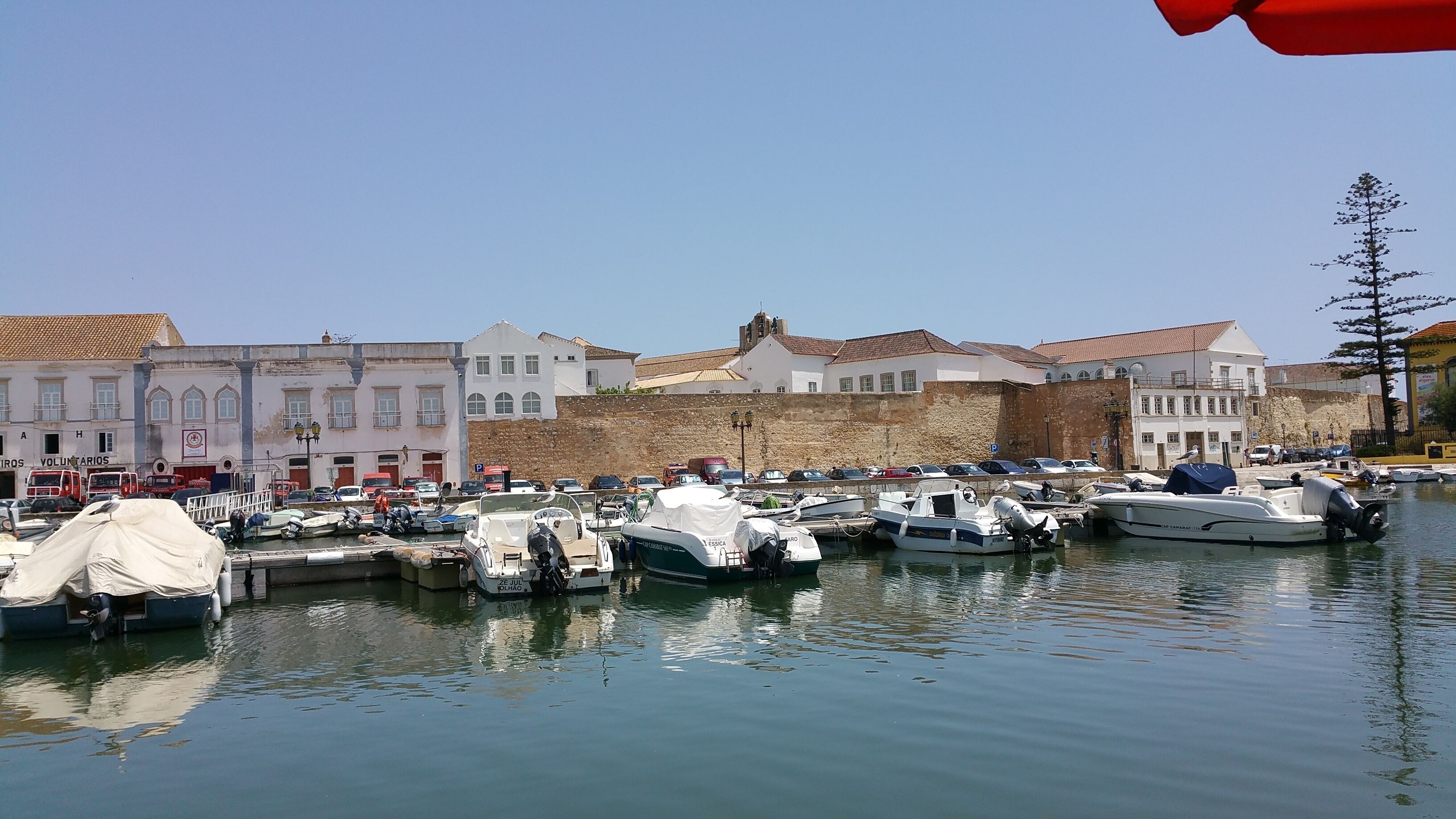 A marina with boats docked, a stone wall, and buildings with traditional architecture.