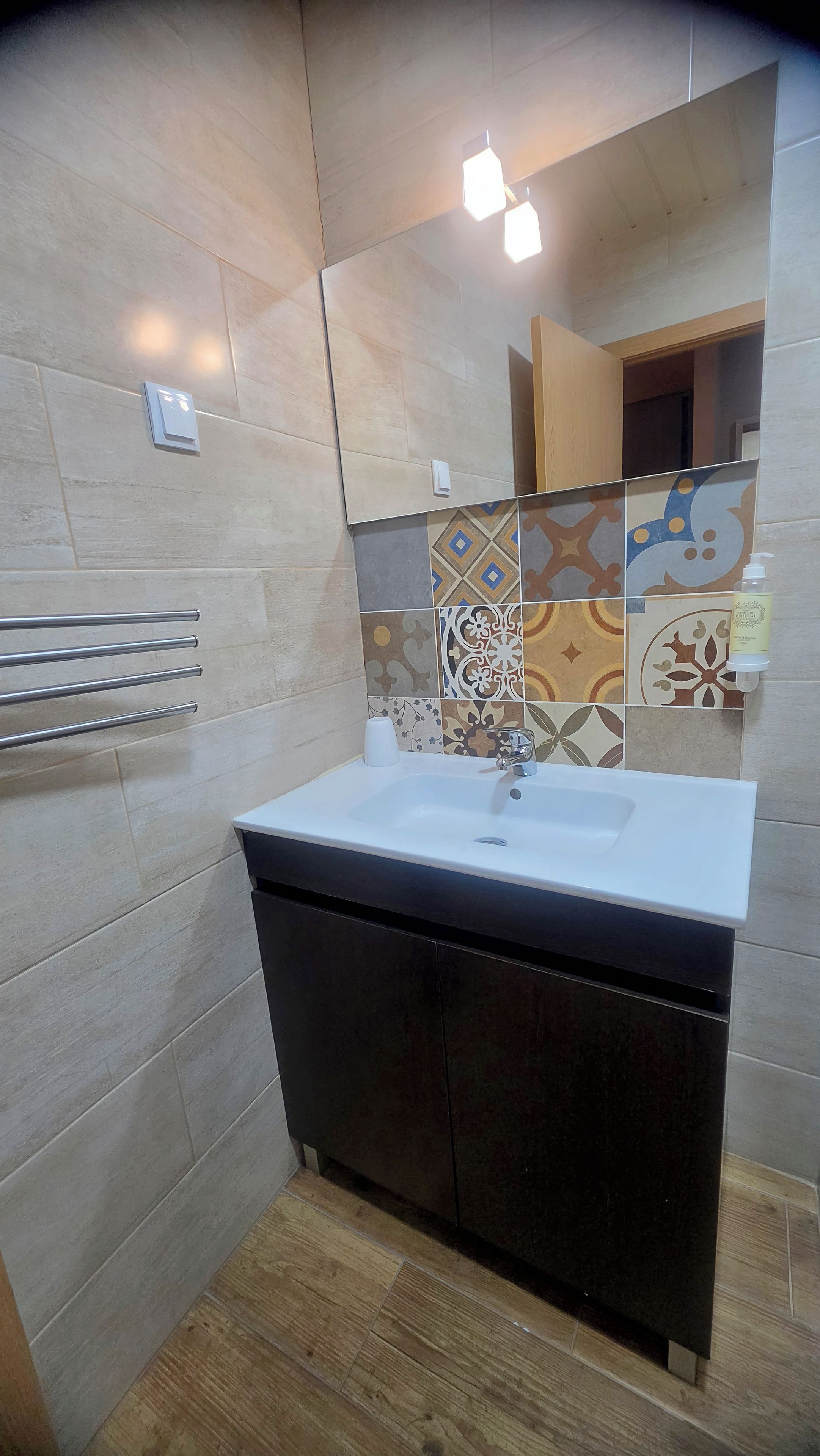 A bathroom with a white sink, dark cabinet, tiled walls, and a mirror.