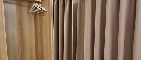 A hotel room with a wooden wardrobe, a bed with a quilted mattress, and beige curtains.