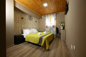 Habitación de hotel con techo de madera, cama con colcha amarilla, un reloj en la pared y ventana con cortina floral.