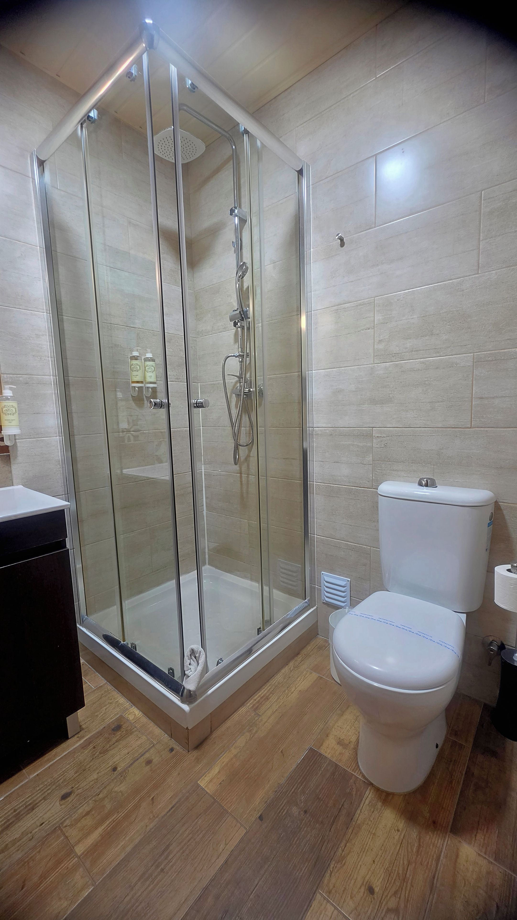 Un baño moderno con ducha envuelta en vidrio, inodoro blanco y suelo de madera.