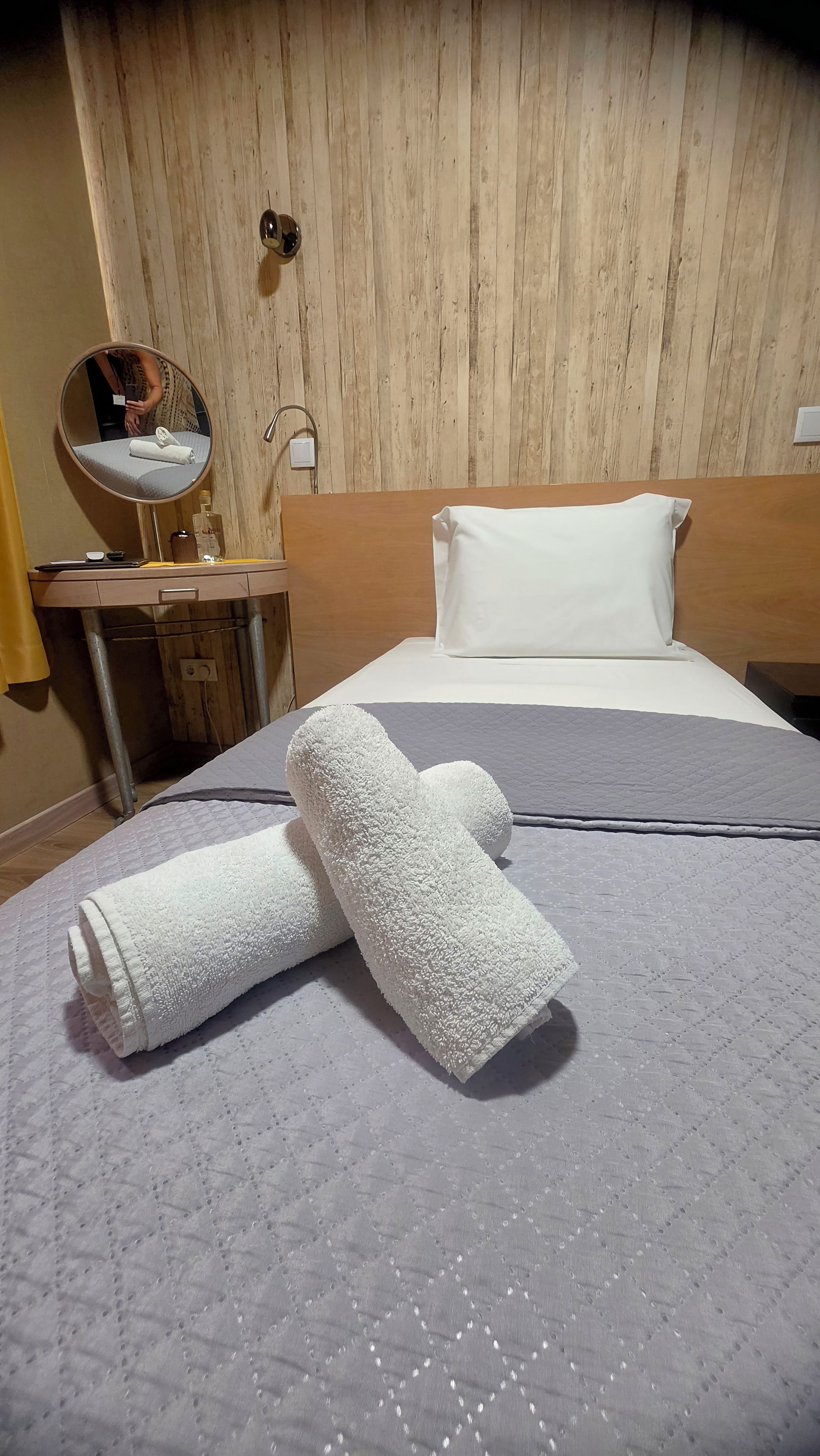 Una habitación de hotel con una cama, una mesita de noche, un espejo y un cabecero de madera.