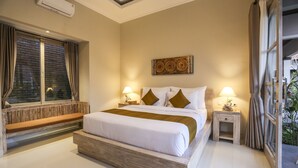 A bedroom with a large bed, two bedside tables with lamps, a window with curtains, and a wall-mounted air conditioner. - Uma Dhari Villa (Sukawati)
