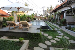 A pool area with lounge chairs and umbrellas, surrounded by a garden with stepping stones and various plants. - Uma Dhari Villa (Sukawati)