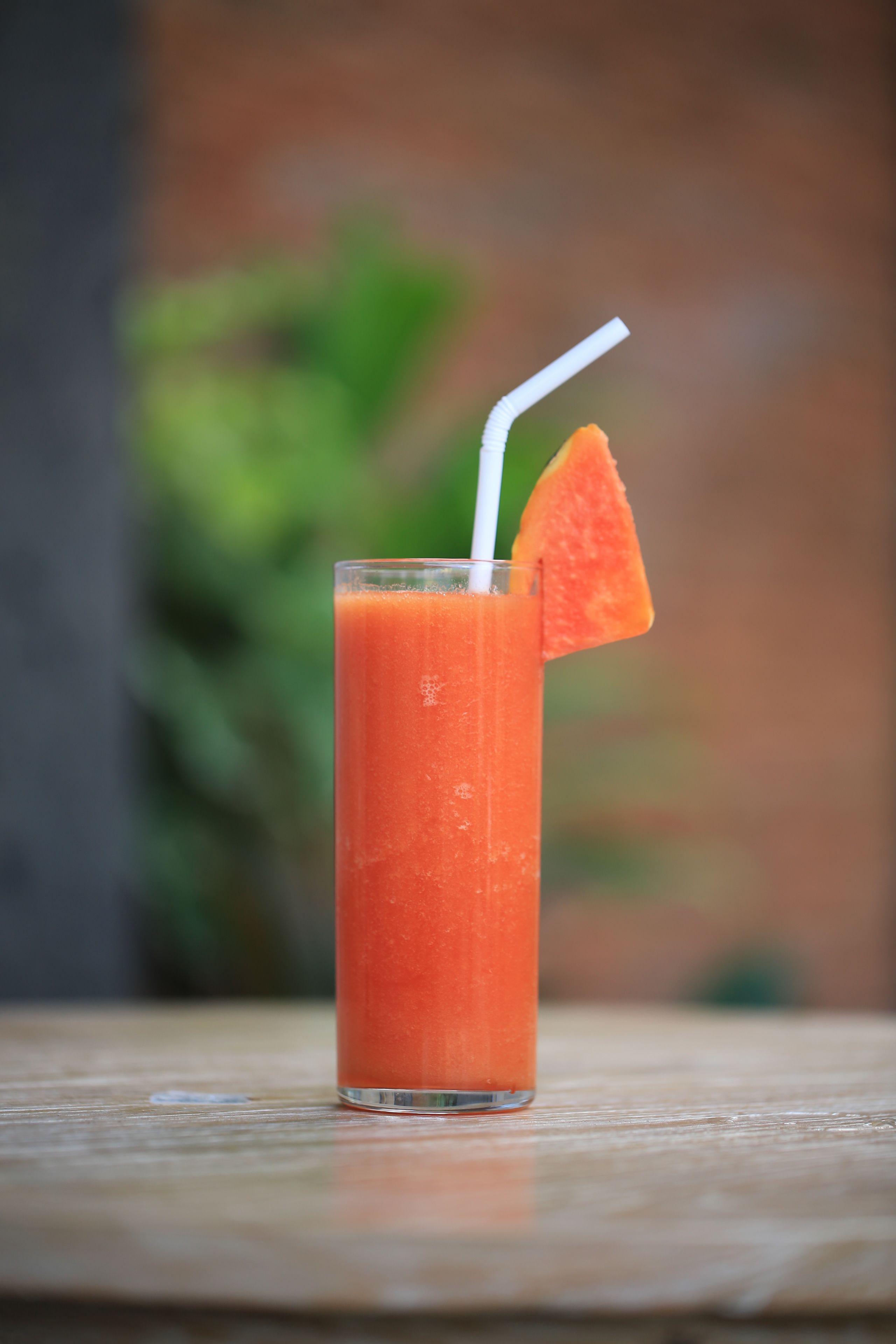 Un grand verre de jus d’orange, avec une paille et une tranche d’orange sur le bord, posé sur une surface en bois.