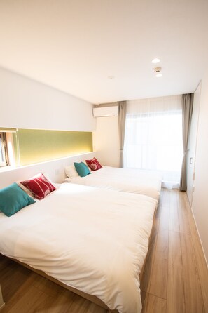 A hotel room with two beds, a large window with curtains, and a wooden floor.
