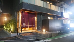 A modern building with a prominent entrance, a red curtain, and a small outdoor area with steps leading up to the door. - Apartment Hotel Tenjin Tumugu (Fukuoka)