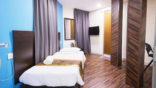 A hotel room with a blue accent wall, a wooden floor, a bed with white bedding and a gold accent, a flat-screen TV, and a door with a wooden panel design. - Hotel Sunjoy9 OKR Near Midvalley 10 Mins Only (Kuala Lumpur)