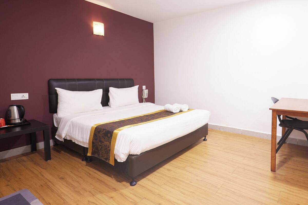 A hotel room with a bed, bedside table, and a small desk with a chair.